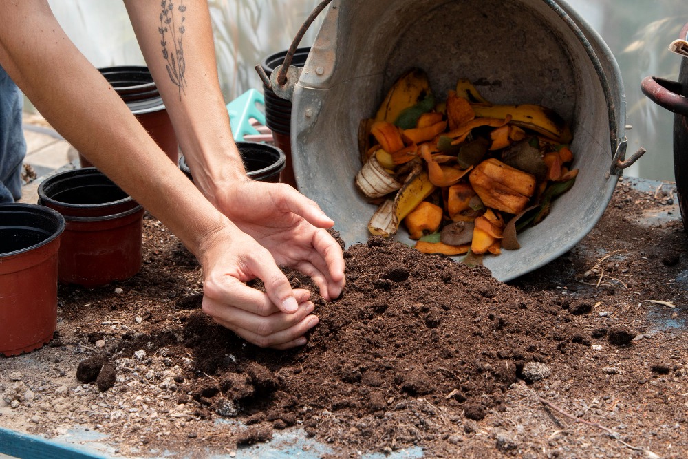 Mãos mexendo na terra com um balde com resíduos orgânicos ao lado